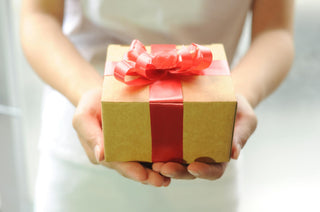 Person holding a small gift box with a red ribbon against a neutral background