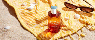 Bottle of perfume on a yellow towel with sunglasses and seashells on a sandy background